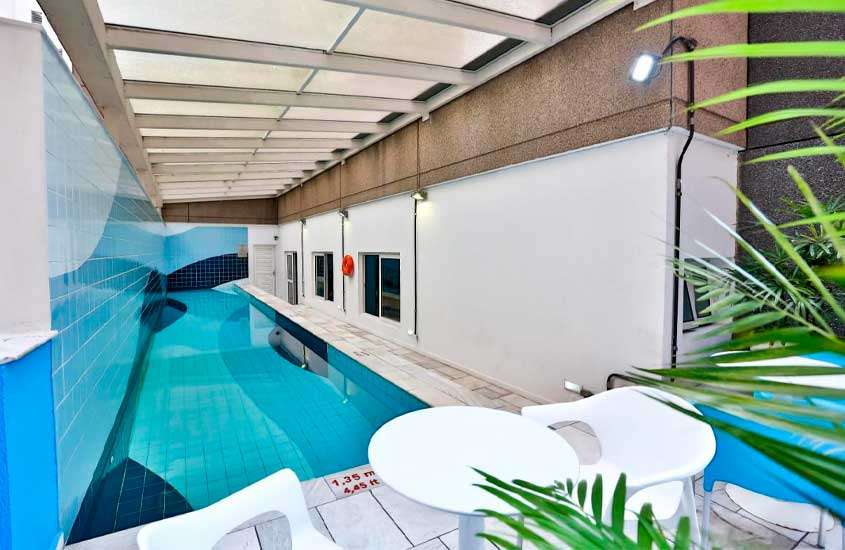 Área de lazer interna de hotel em são paulo com piscina, mesas, cadeiras e plantas decorativas