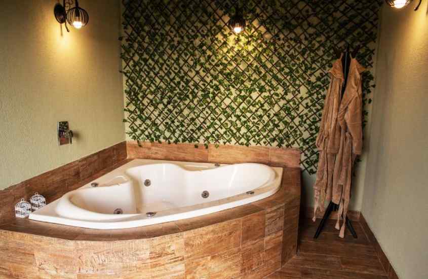 Banheira de hidromassagem de um hotel romântico em Águas de lindóia com roupões e parede verde de plantas decorativas atrás