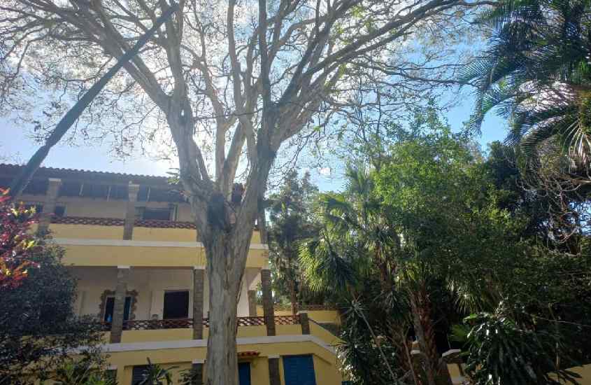 Em um dia de sol, fachada de um dos hotéis fazenda em Miguel Pereira com várias árvores na frente