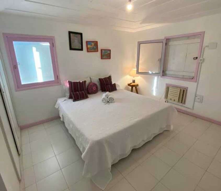 Quarto de hostel em búzios com cama de casal, toalhas, quadros decorativos, ar condicionado, luminária e janelas grandes