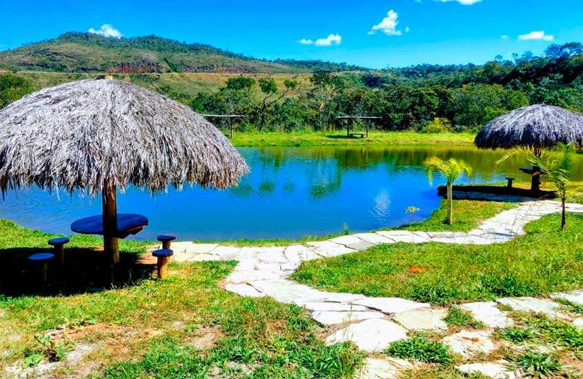 Em um dia ensolarado, lago de hotel fazenda perto de brasília com mesas, bancos, área gramada e árvores ao redor