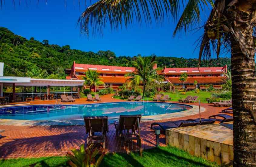 Durante um dia de sol, área de lazer de um dos melhores hotéis fazenda perto de ribeirão preto com piscina, espreguiçadeiras, hotel e vegetação ao redor