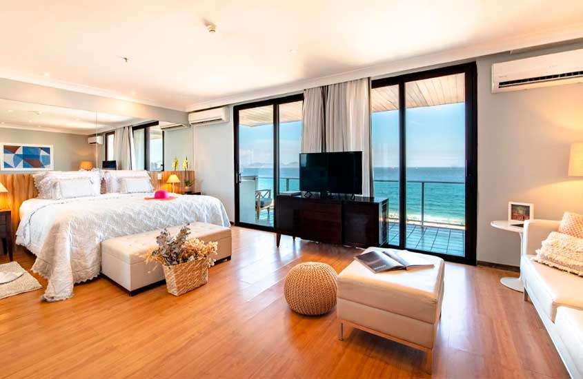 Em um dia ensolarado, quarto de um hotel em copacabana beira mar com cama de casal, TV, ar-condicionado, sofás e janelas grandes acortinadas