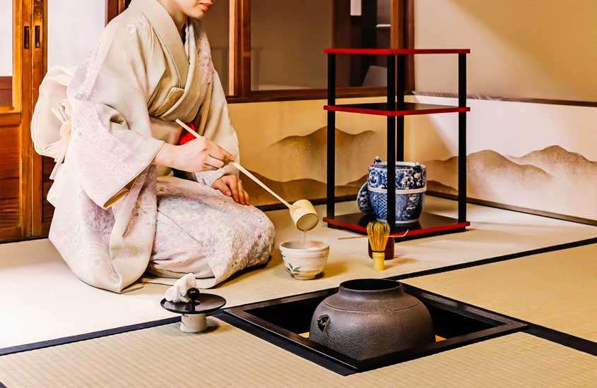 Durante a cerimônia do chá, mulher servindo o chá, vaso decorativo em pequena estante e janela atrás
