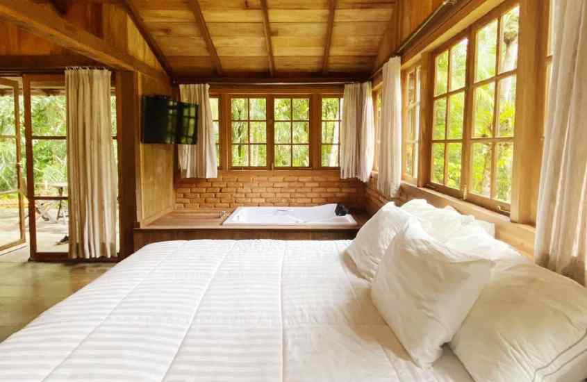 Quarto de hotel com cama de casal, hidromassagem, TV e estrutura de madeira