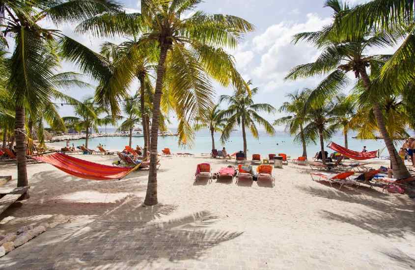 Em um dia de sol, praia privativa de um resort em curaçao com redes, cadeiras, espreguiçadeiras, árvores e mar na frente
