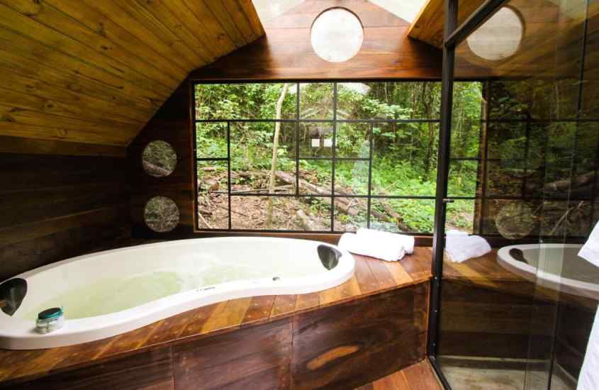 Banheiro de um dos hotéis fazenda perto de ribeirão preto com banheira de hidromassagem, deck de madeira, janela grande, toalhas e box lateral
