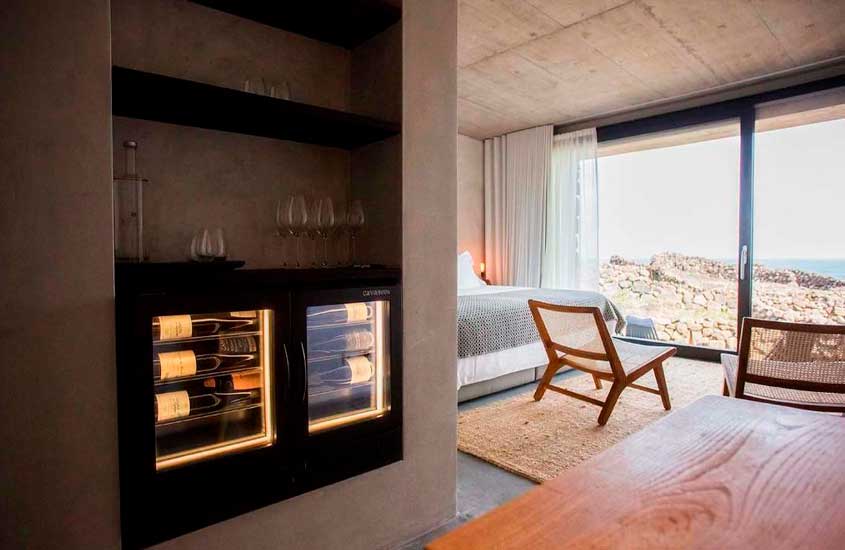 Durante um dia de sol, quarto de um dos hoteis vinícolas em portugal com cama de casal, poltronas, tapetes, adega, mesa de apoio e janelas grandes