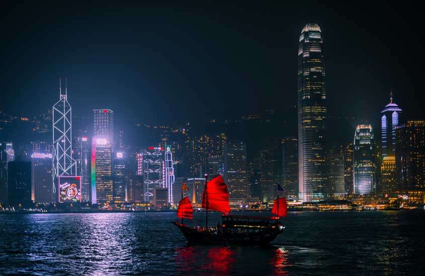 Durante a noite, bairro onde ficar em Hong Kong com barco no mar e prédios atrás