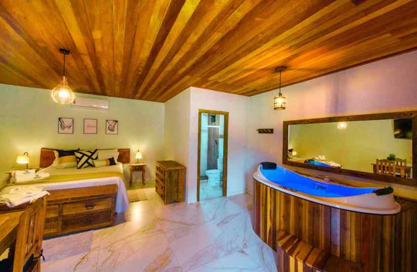 Quarto de hotel com cama de casal, banheira de hidromassagem em deck de madeira, banheiro e espelho