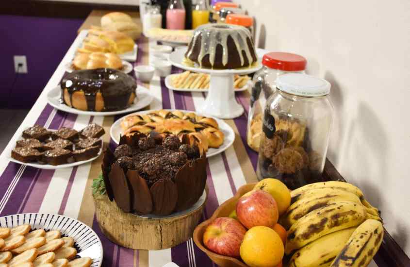 Mesa de café da manhã de hotel farta com bolos, frutas, biscoitos e bebidas