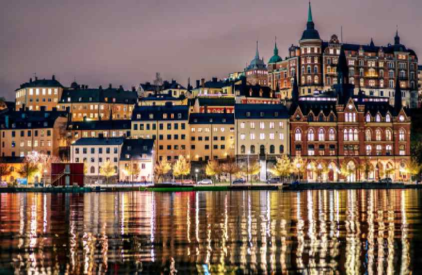 Durante o anoitecer, prédios iluminados refletidos no mar em Södermalm, um bairro onde ficar em estocolmo