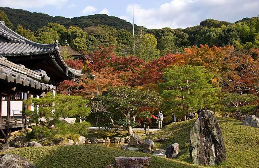 Em um dia de sol, templo em kyoto com muita vegetação ao redor, lago e pessoas visitando
