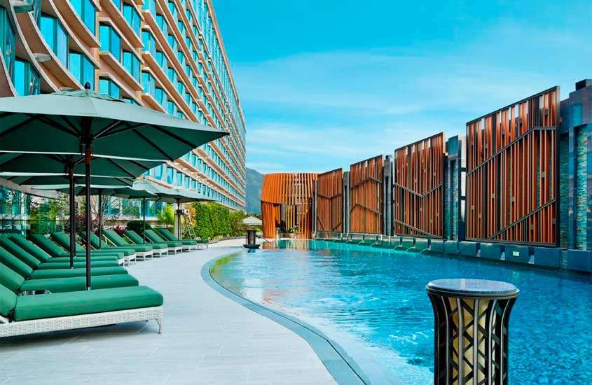 Em um dia de sol, área de lazer de um dos melhores hotéis em Hong Kong com piscina, espreguiçadeiras, guarda-sóis, hotel do lado e decorações de metal