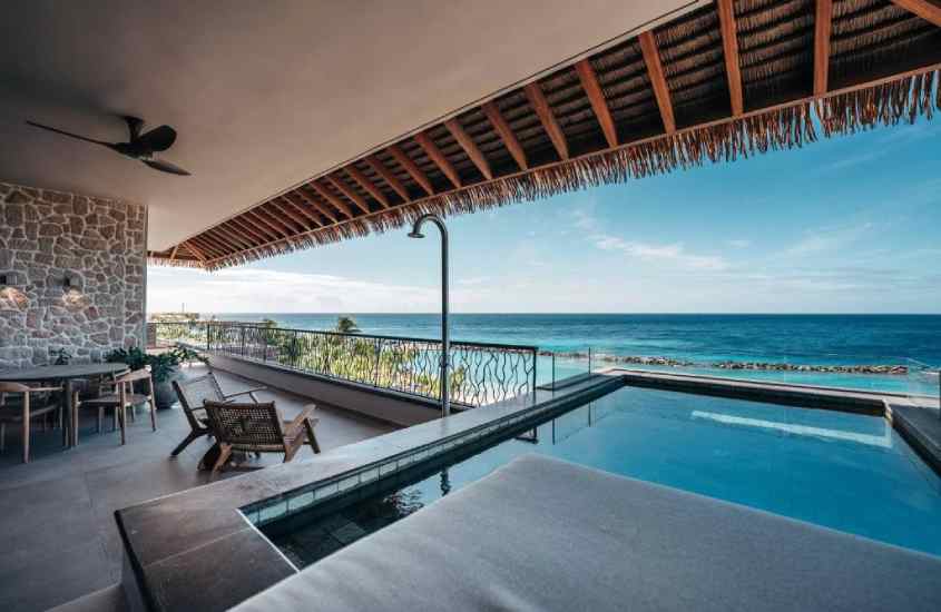 Em um dia ensolarado, varanda de um dos melhores hotéis em curaçao com cadeiras e mesa de madeira, piscina privativa, ducha e vista para o mar