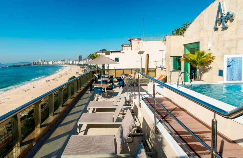 Durante um dia de sol, área de lazer de um hotel em copacabana rio de janeiro beira mar com espreguiçadeiras, mesas, guarda-sóis, piscina, hotel do lado e litoral na frente