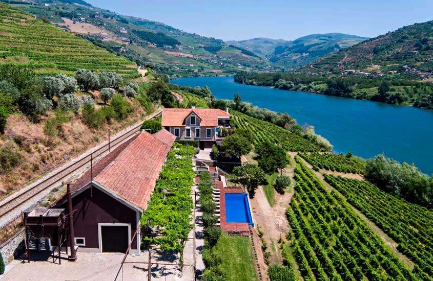 Em um dia de sol, vista aérea de um dos melhores hoteis vinicolas portugal com piscina, vinícolas, parreiras e rio do lado