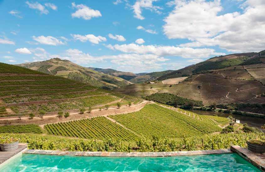 Em um dia de sol, área de lazer de um dos melhores hoteis vinicolas portugal com piscina e paisagem da vinícola na frente