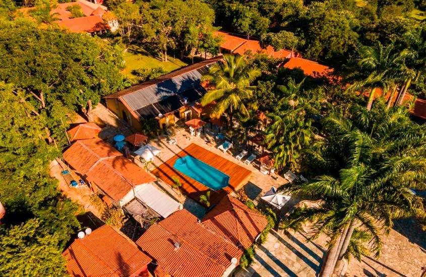 Em um dia de sol, vista aérea de um hotel fazenda perto de brasília com piscina, espreguiçadeiras e árvores ao redor