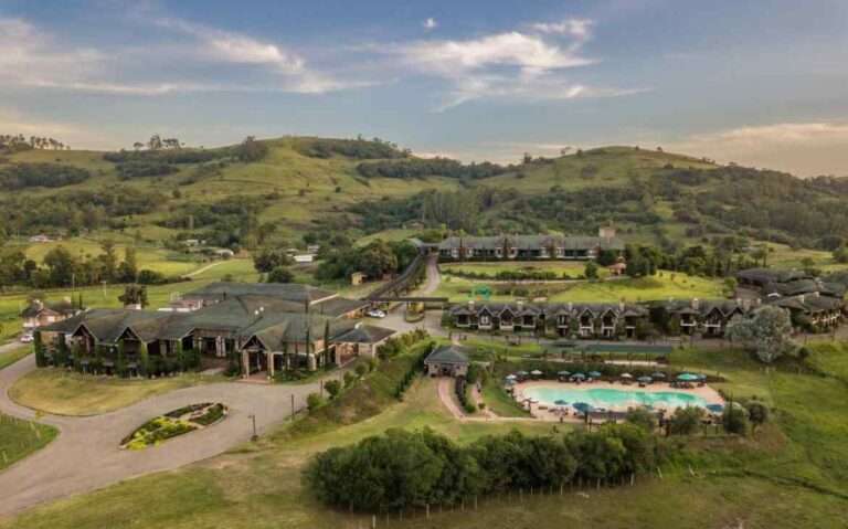 Durante o entardecer, vista aérea de um dos hotéis fazenda no rio grande do sul com bastante área verde, montanhas e piscinas grandes