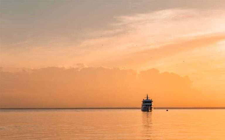Em um dia de sol, navio no meio do mar que reflete o céu alaranjado com roxo