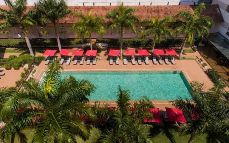 Em um dia de sol, vista aérea do hotel Vila Gale Rio de Janeiro com piscina, espreguiçadeiras, guarda-sóis e árvores ao redor
