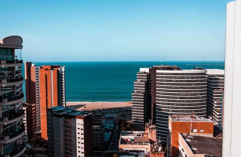Em um dia de sol, vista aerea de Fortaleza, um lugar barato para passar o ano novo com prédios ao redor e mar na frente