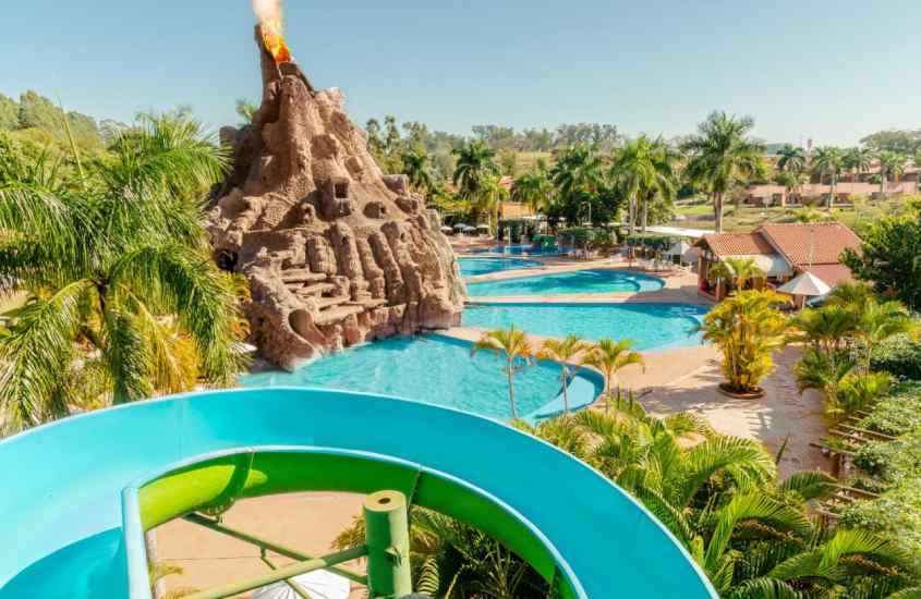 Em um dia de sol, área de lazer de um dos resorts para passar o ano novo com piscinas, toboágua, vulcão decorativo e árvores ao redor