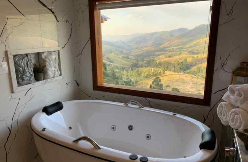 Durante uma manhã de sol, banheira de um hotel com janela grande com vista das montanhas, toalhas e armário ao lado