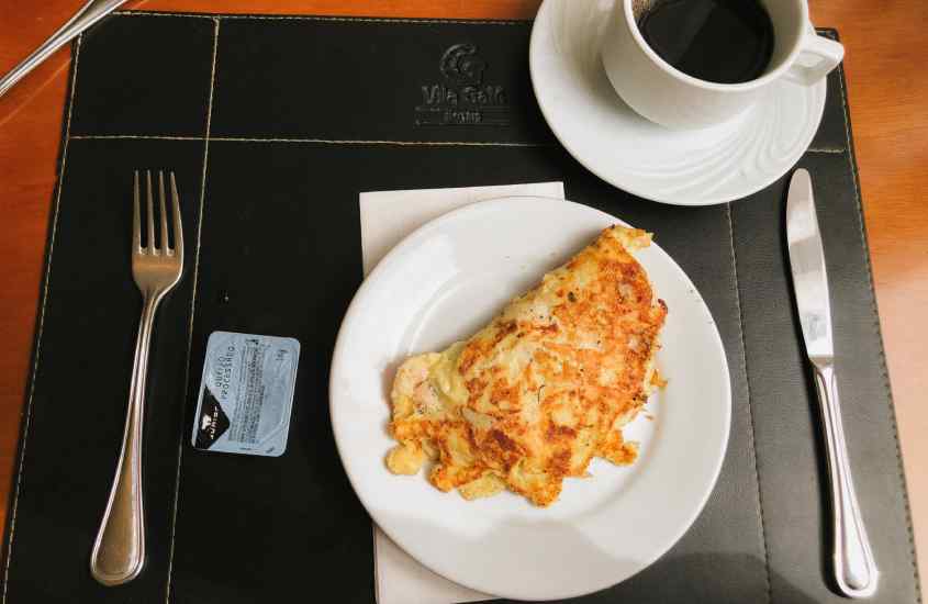 Mesa de café da manhã com omelete, garfo, jogo americano preto, faca e café preto