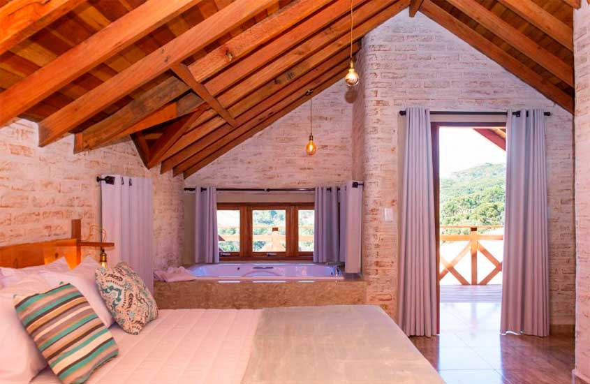 Quarto de um dos chalés com hidro em monte verde, com cama de casal, janelas de madeira, varanda e aquecedor