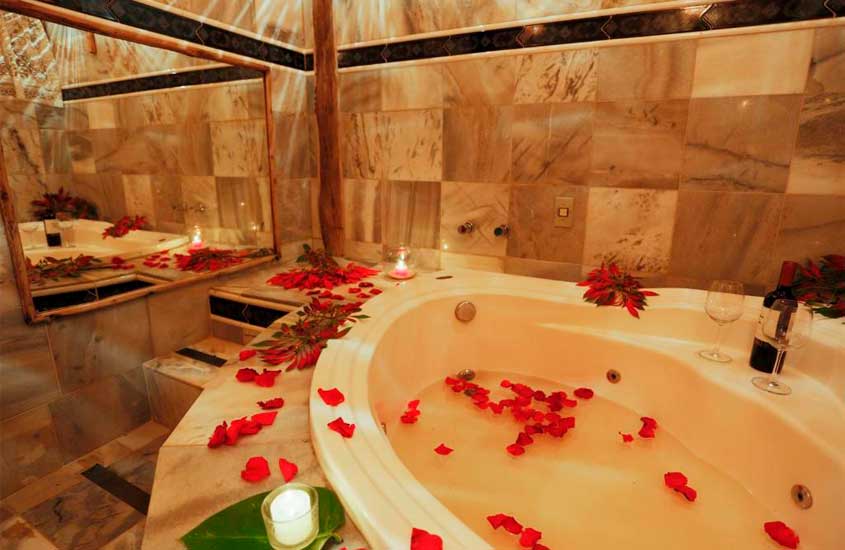 Banheira de um dos chalés com pétalas de rosa, vinho com taças, velas, espelho e piso frio
