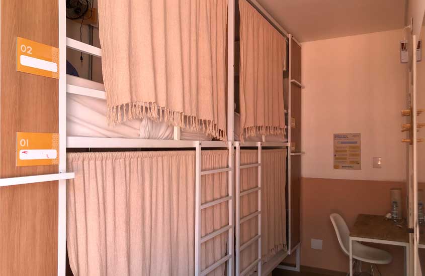Interior de um quarto compartilhado no hostel angatu com camas acortinadas e estação de trabalho