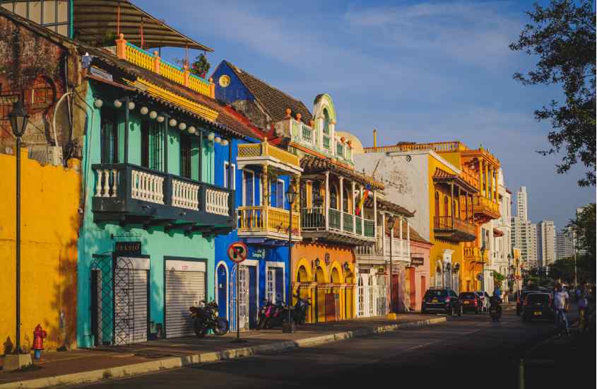 Em um dia de sol, rua com casas coloridas em Cartagena das Índias com pessoas e carros passando