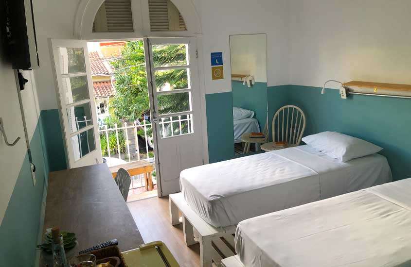 Quarto privativo do hostel angatu com camas, estação de trabalho, janela grande, TV, espelho, cadeira de apoio e frigobar