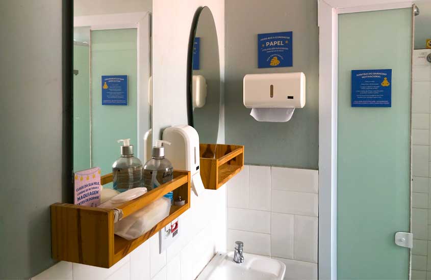 Interior do banheiro do angatu hostel com pia, espelhos, lenço umidecido, sabonete, alcoól em gel e lenços de papel