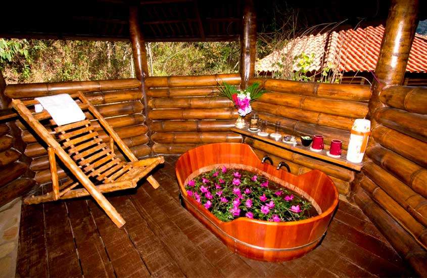 Área de banheira de uma das melhores pousadas em são thomé das letras com cadeira de madeira, prateleira com copos, xícaras, café e flores decorativas