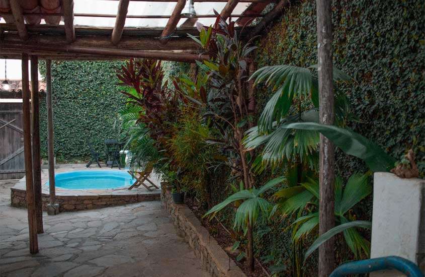Área de lazer de uma das pousadas em Diamantina com piscina, mesas, cadeiras, plantas decorativas e parede gramada ao redor