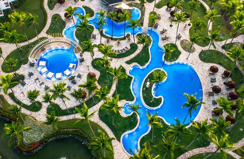 Vista aérea de um dos resorts para passar o ano novo com piscinas, área verde, muitas árvores, mesas, cadeiras e tendas de palha