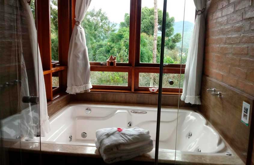 Banheira de um dos chalés em monte verde com hidro, janelas grandes de madeira e toalhas