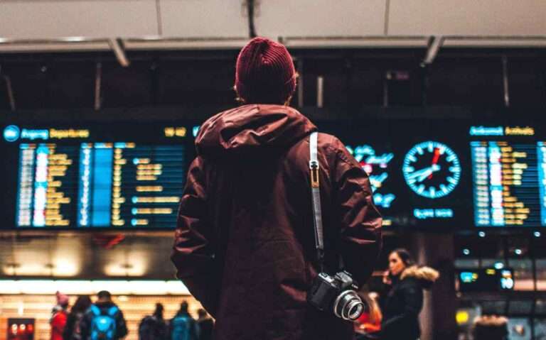 Pessoa de costas com roupas de frio em aeroporto olhando o painel de horários