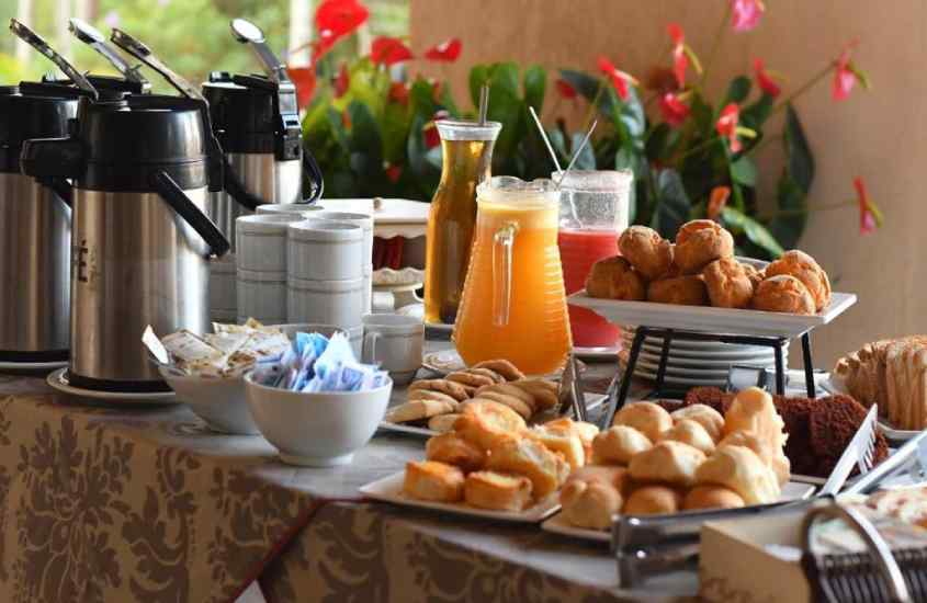 Mesa de café da manhã de um hotel fazenda em serra negra com sucos, pães, bolos, cafés e flores atrás
