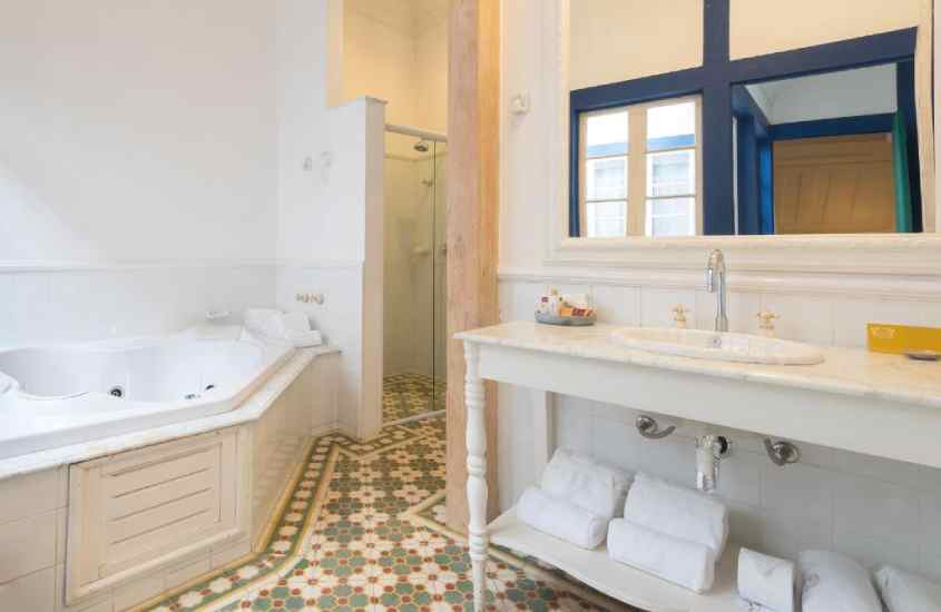 Banheiro de uma pousada em ouro preto com banheira, chuveiro, espelhos, toalhas, pia e amenities