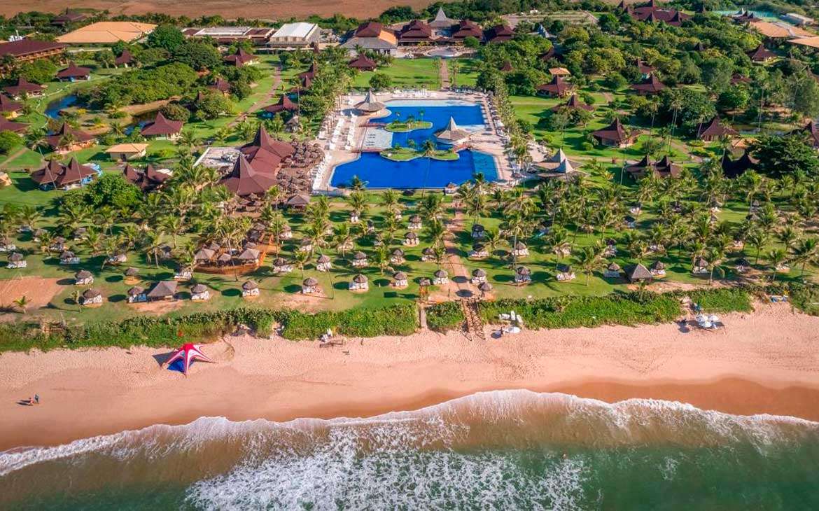 Em um dia de sol, vista aéres de um resort para passar o carnaval com mas na frente, piscinas, árvores e tendas ao redor