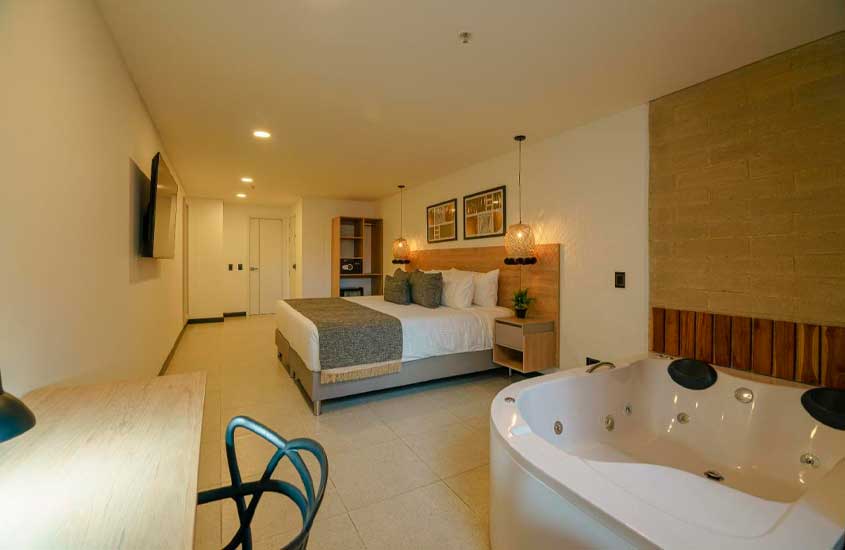 Quarto de um dos hotéis onde ficar em medellin com área de trabalho, banheira, cama de casal TV e quadros decorativos