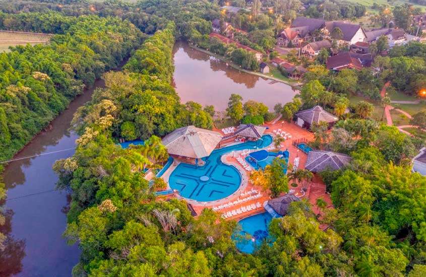 Em um dia de sol, vista aérea de um resort para o carnaval com piscinas, espreguiçadeiras, árvores e rio ao redor