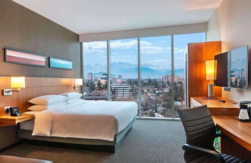 Quarto de hotel em santiago do chile com cama de casal, estação de trabalho, TV e janela grande com paisagem da cidade