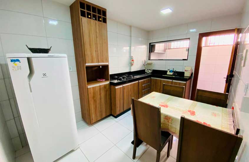 Cozinha de uma casa em Guarapari com mesa, cadeiras, armários e geladeira.