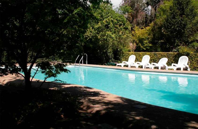 Em um dia de sol, área de lazer de um hotel em santiago do chile com piscina, espreguiçadeiras e árvores ao redor