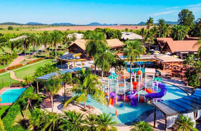 Durante uma manhã de sol, área de lazer de um resort para o carnaval com piscinas, brinquedos aquático, árvores e parte gramada e plantas ao redor